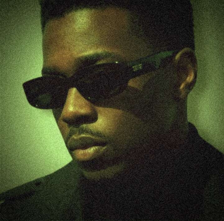 Close portrait of K.R.W.N. wearing sunglasses in green cinematic light